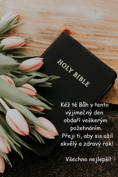 Přání k narozeninám pro křesťany na pozadí bible překryté tulipány v lososové barvě.