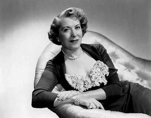 Černobílá fotografie Gracie Allen sedící na gauči. 