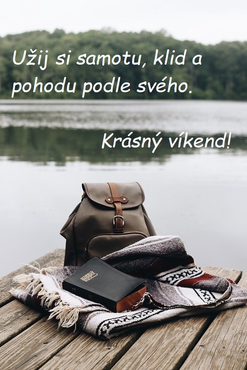 Pohled na jezero u mola, na němž je batoh, deka a kniha.