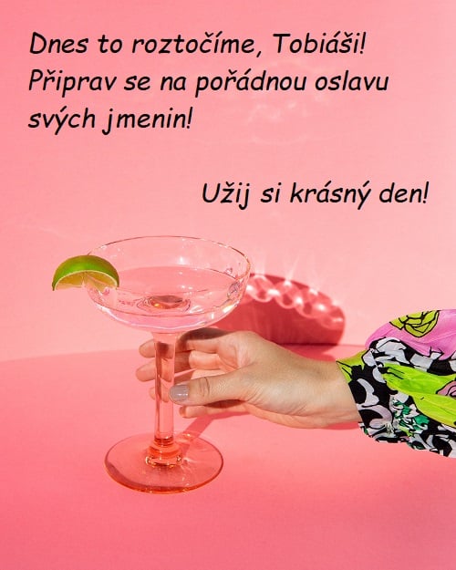 Dámská ruka držící drink s limetkou a přáním krásného dne a oslavy jmenin. 