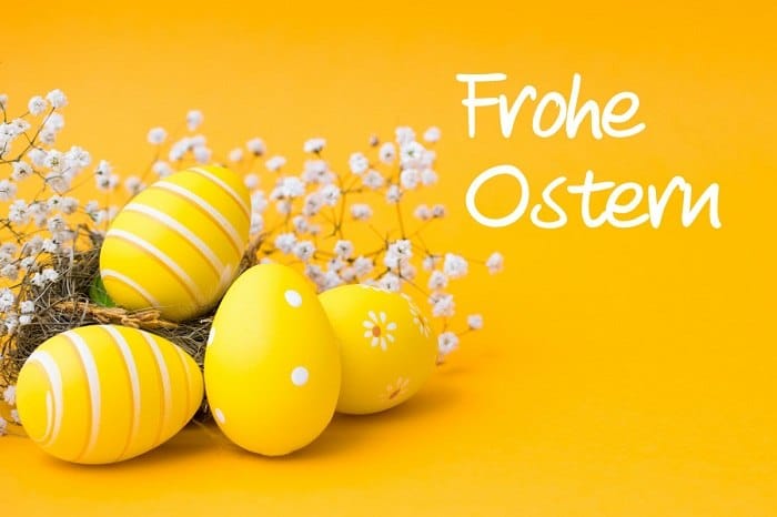 Krásná žlutá malovaná vejce na žlutém pozadí s květy a nápisem Frohe Ostern.